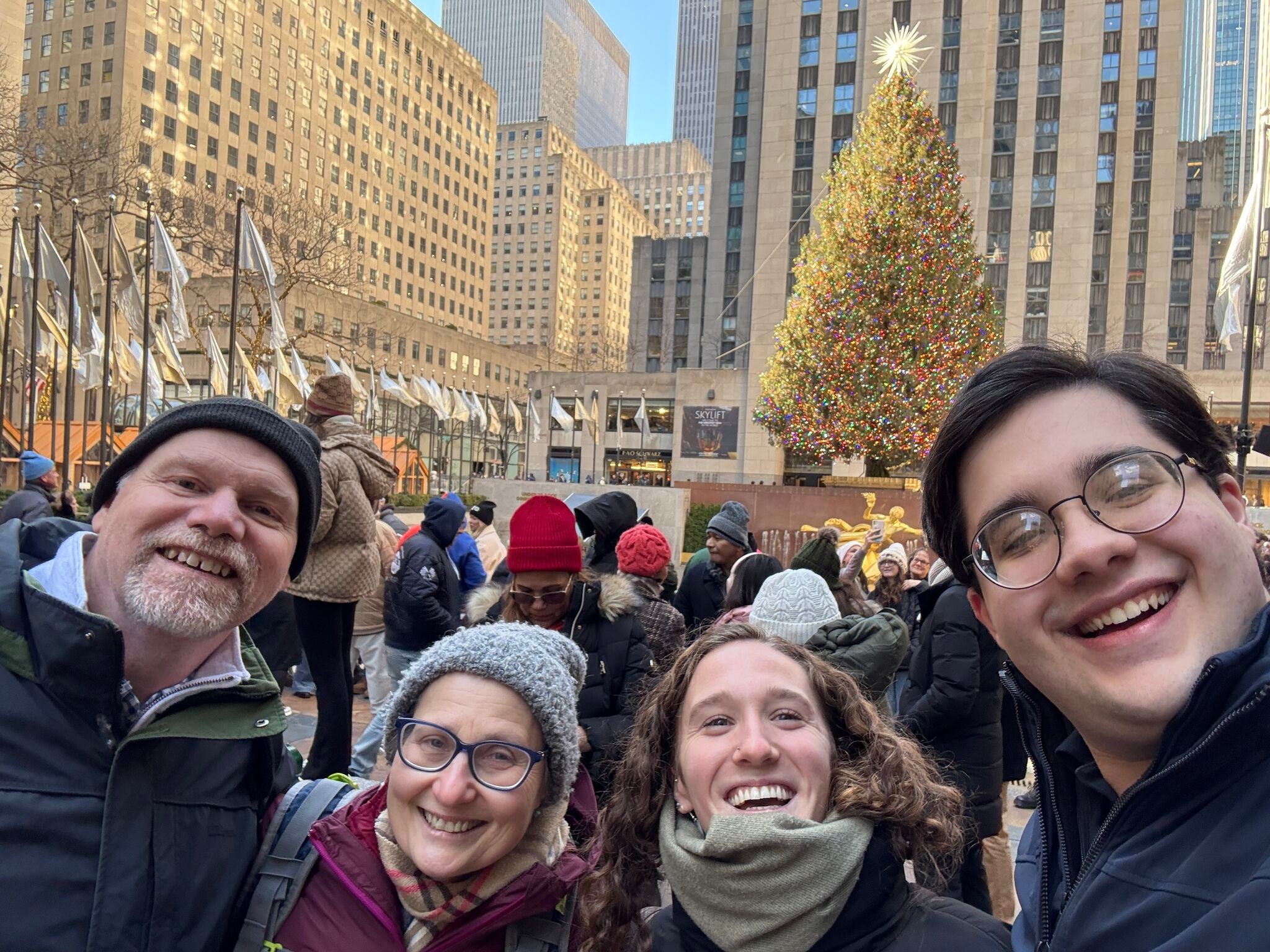 two professors and two students pose in front of the New York City Christmas tree on their trip to present at the American Historical Society.