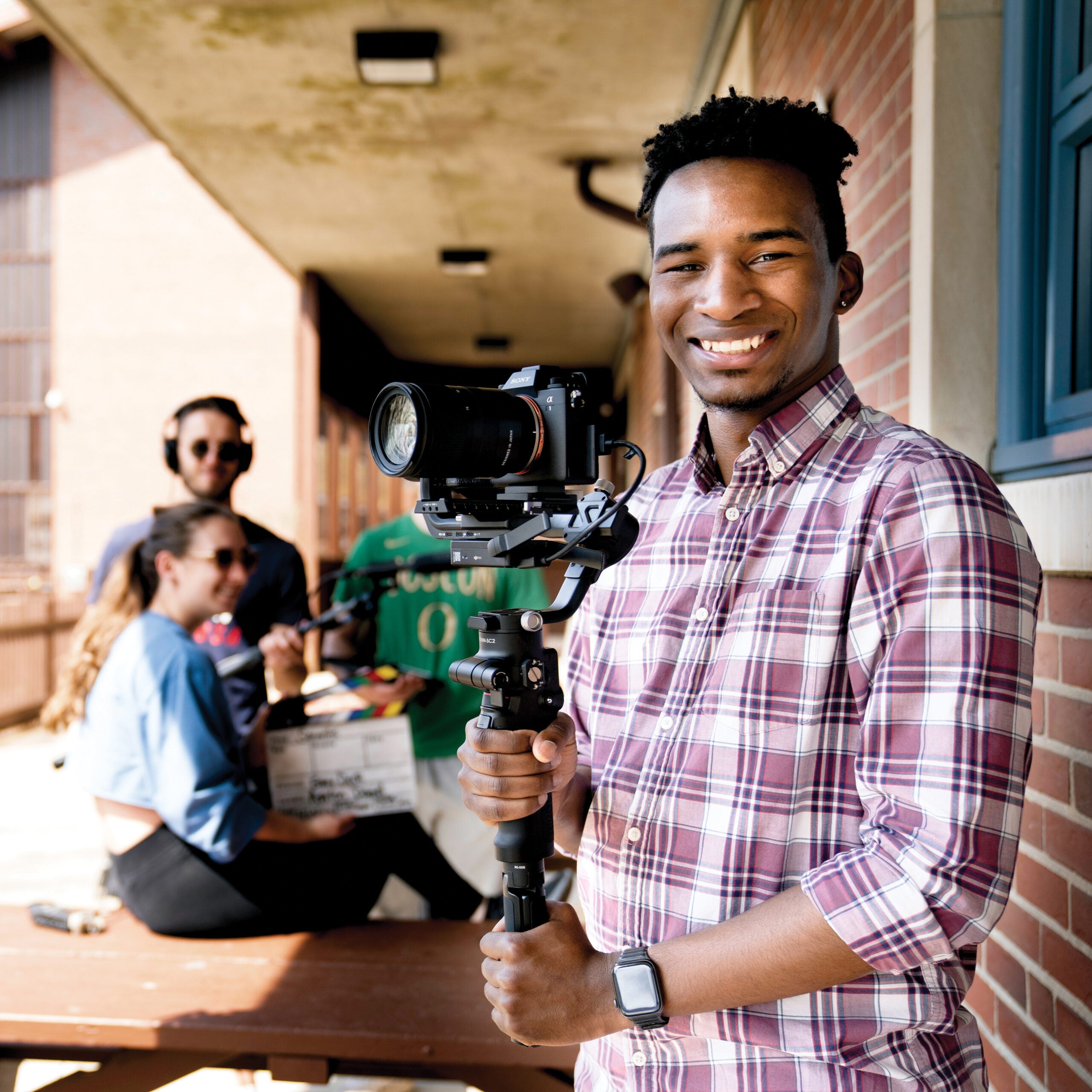 Student holding a camera on set with the crew behind him. 