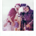 Two male presenting students behind a film camera