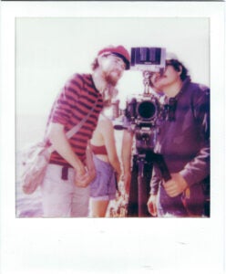 Two male presenting students behind a film camera