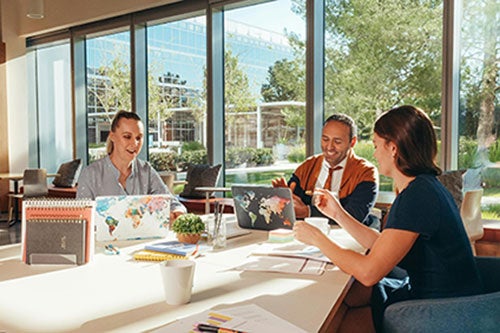 3 adult faculty members, 2 female and 1 male, sit around a table in conversation.