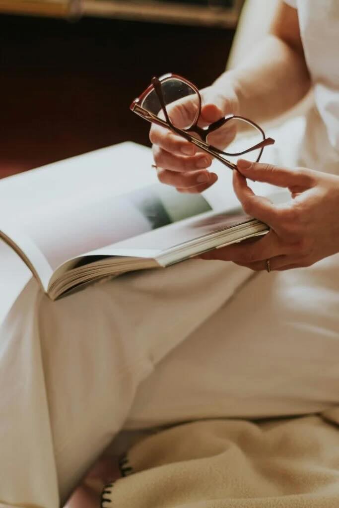 A persons hands holding a book and eyeglasses