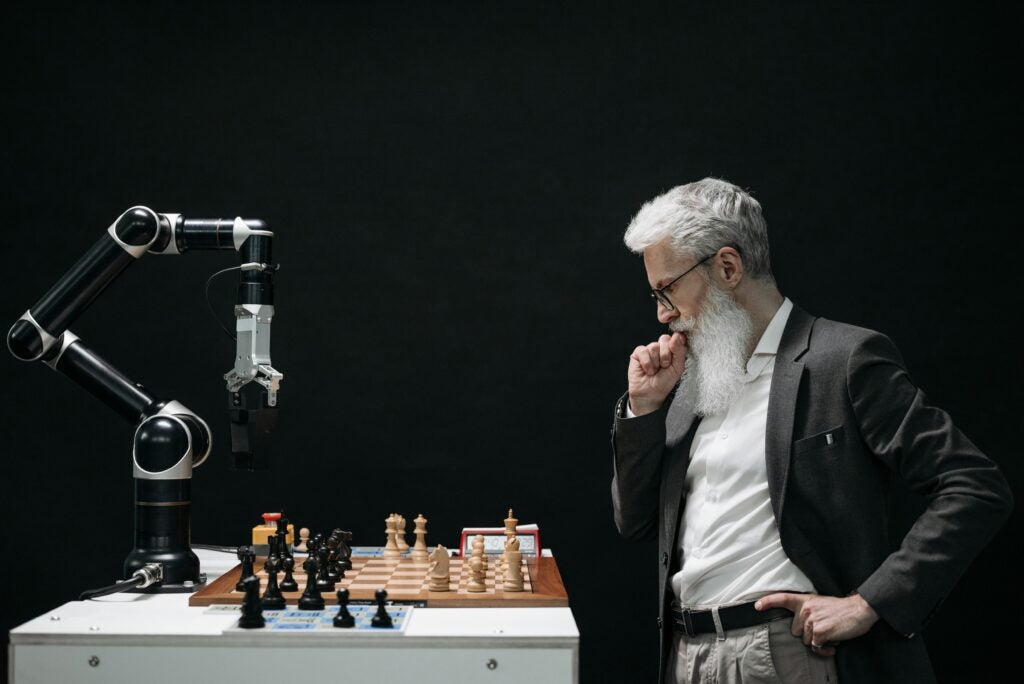 Older man playing chess with AI driven robotic arm