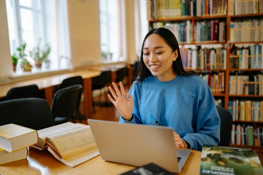Woman at the library waving at people on her laptop.