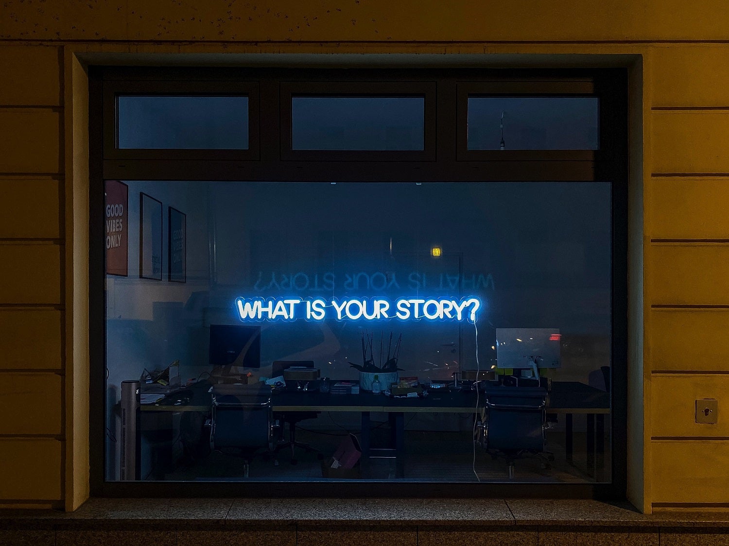 neon lights that say what is your story through a window