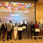 URI Students standing on a stage in front of a digital screen