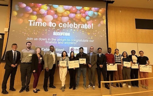 URI Students standing on a stage in front of a digital screen