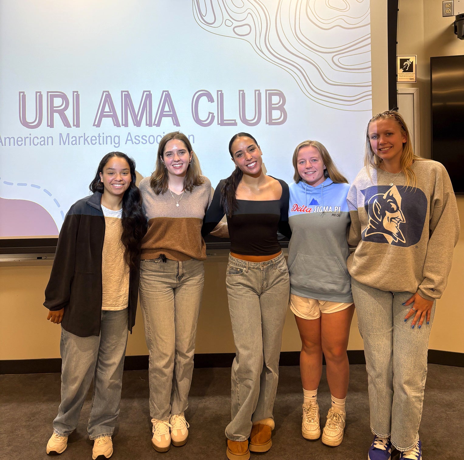 URI Business students standing in front of a screen that says "URI AMA Club"