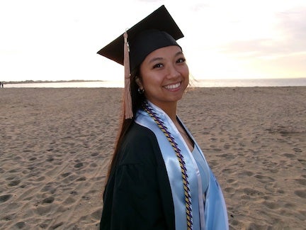 URI college of business student wearing a graduation gown and cap, with the beach as a background.