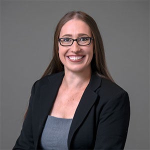 woman smiling wearing glasses, a gray shirt and black blazer