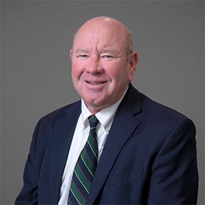 man smiling wearing a blue suit, white shirt and green stripped tie