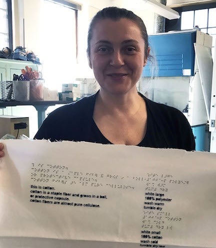 URI TMD Professor is holding up white fabric with braille writing on it