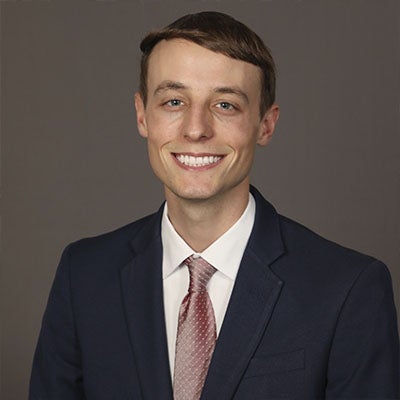 URI student smiling wearing a blue suit jacket and pink tie