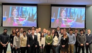 a group of URI College of Business students standing in front of large drop-down screens, at Fidelity.