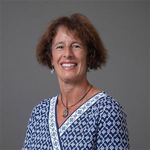 woman smiling wearing a necklace and patterned blue shirt