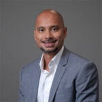 man smiling wearing a light grey suit jacket and white shirt