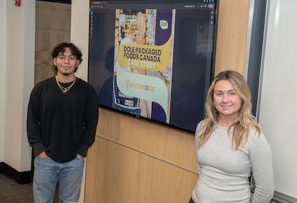 Two URI College of Business students standing against a wall that has an image on it