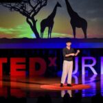 TEDxURI event with a person on the stage and giraffes on the screen behind him