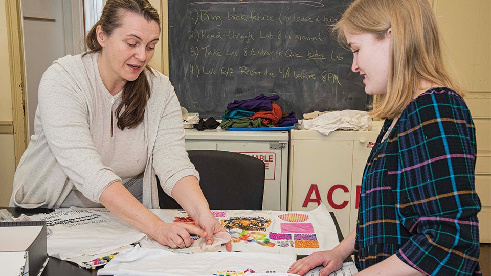 URI TMD professor and URI student pointing to fabric samples on a table