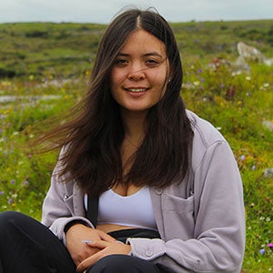 URI student smiling, sitting down in a field of green