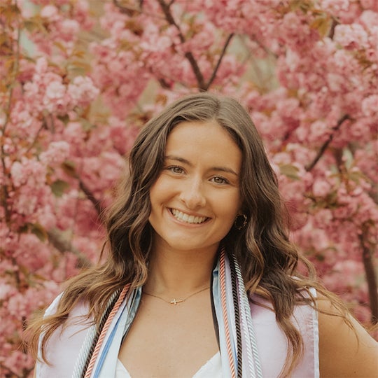 URI College of Business Student smiling with a background of a flowering tree.