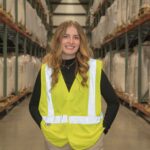 Emily Fischer standing in a warehouse wearing a yellow vest