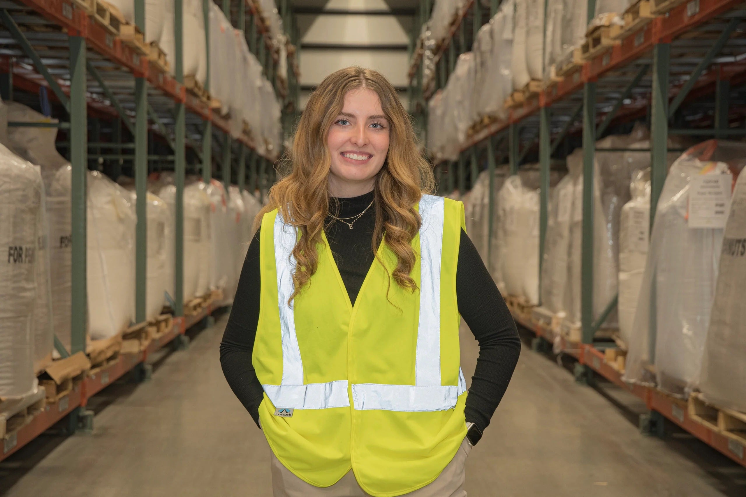 Emily Fischer standing in a warehouse wearing a yellow vest