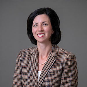 woman smiling wearing a brown jacket and white shirt