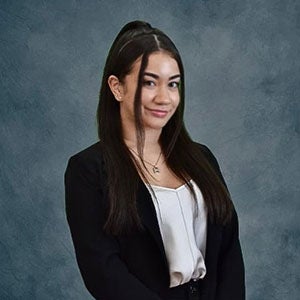 URI student with long dark hair, wearing a black jacket and white shirt.