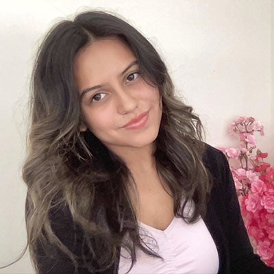 URI student smiling wearing a black suit jacket with pink flowers in the background