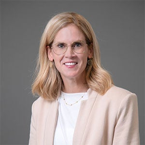 woman smiling in a white shirt and light-colored jacket
