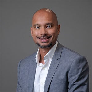 man smiling wearing a light grey suit jacket and white shirt