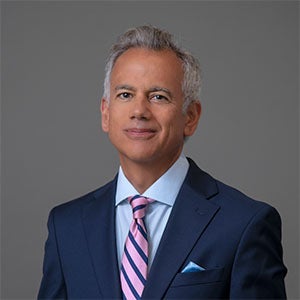 man smiling wearing a blue suit and pink striped tie