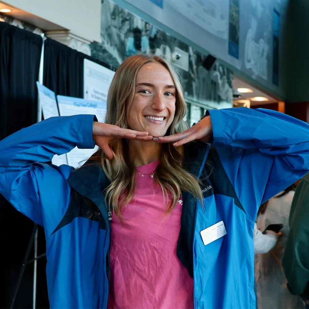 A photo of Harper smiling wearing a blue jacket and a pink shirt