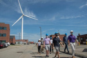 Participants in the Energy Fellows program, in the Cooperative Extension, wearing hard hats and touring a local facility with a wind turbine in the background