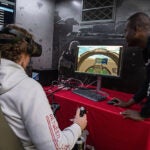 Ethan Sironen, a junior marine affairs major, left, tests his flying skills with a Marine Corps flight simulator as Marine Sgt. Thibault Adjogble looks on