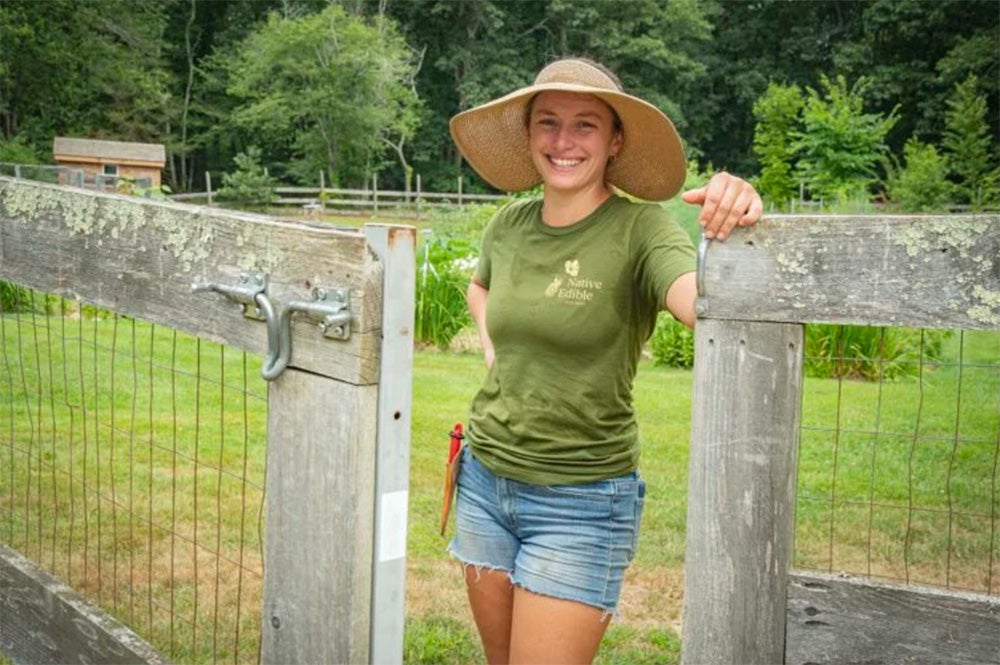 image of URI alumna Cassidy Need ’20 standing in the opening of a garden fence