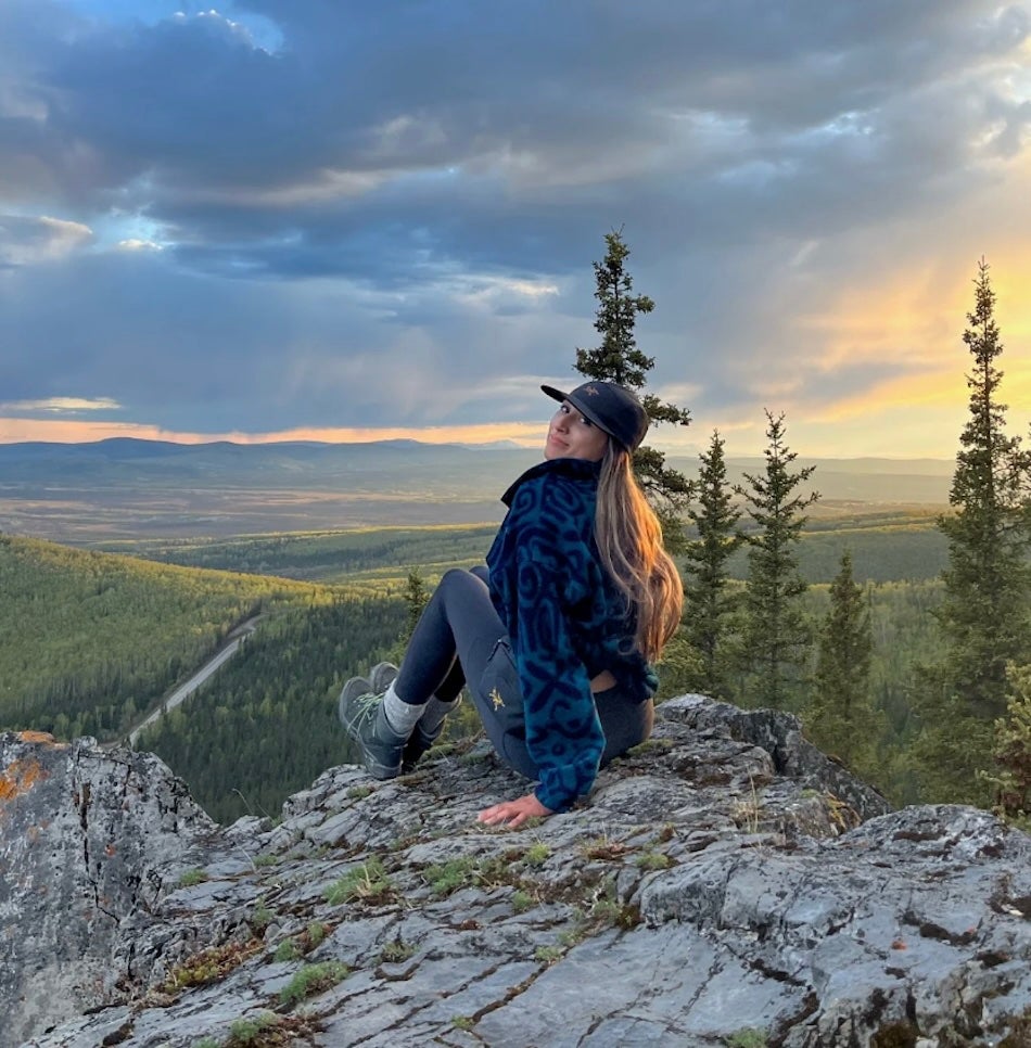 image of CELS Landscape Architecture Aisha Malik sitting on a cliff with a large forest in the background