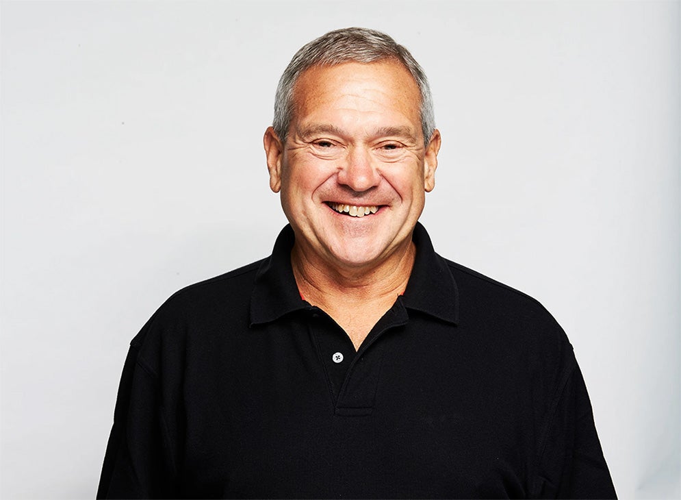 Image of Professor Dennis Nixon smiling wearing a black collared shirt in front of a white background