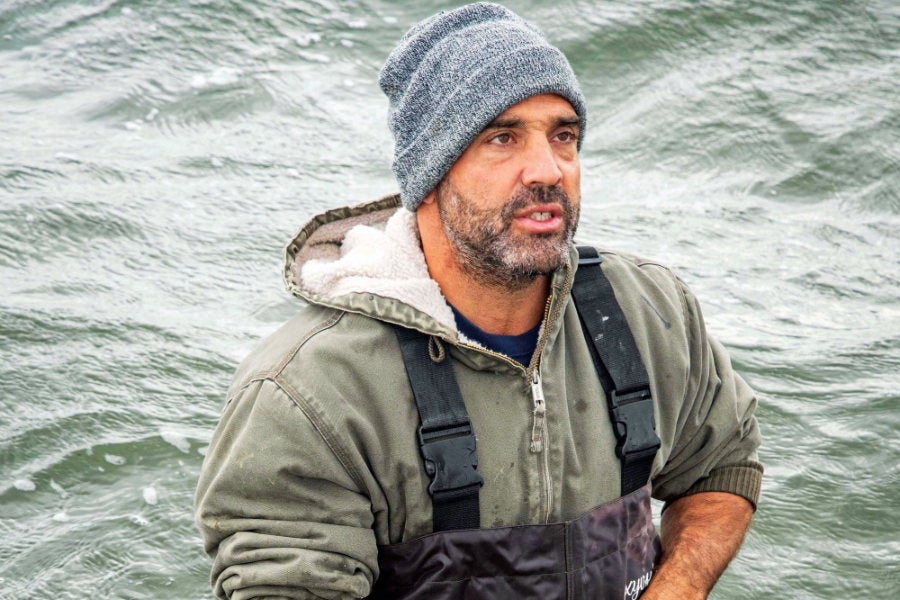 Perry Raso ’02, M.S. ’06, founder and owner of Matunuck Oyster Farm, stands waist-deep in Potter Pond, in South Kingstown, R.I. standing in a cove holding oysters from an oyster farm