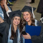 image of two URI graduates smiling after receiving their diplomas. URI photos by Nora Lewis.