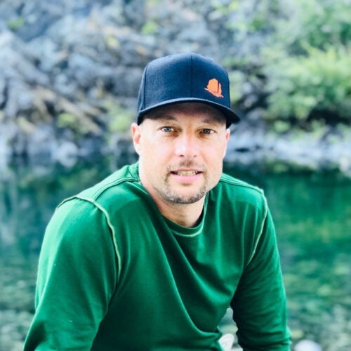 URI water researcher Kyle Young, a Ph.D. candidate in hydrogeology at the University of Rhode Island outdoors in front water, surrounded by rocky terrain.