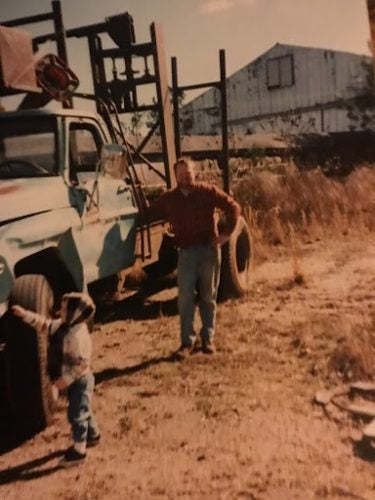 Portrait of the writer as a young logger, standing in a dusty farm landscape next to a pickup truck. Credit: Madison Jones