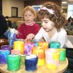 URI Child Development Centers students Lily (right) and Marit display the candleholders they and their fellow preschool students created, along with a host of other artworks, as gifts for donations to the Rhode Island Community Food Bank.