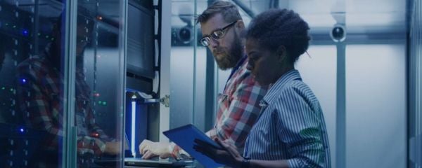 two computer science professionals stand in front of large servers