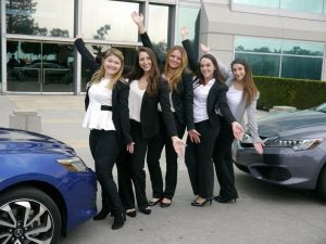 Several students in business attire standing next to two cars.