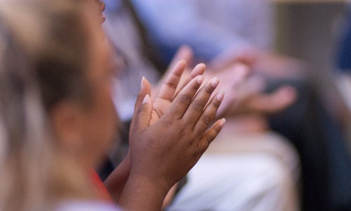 A woman clapping her hands during a URI community announcement