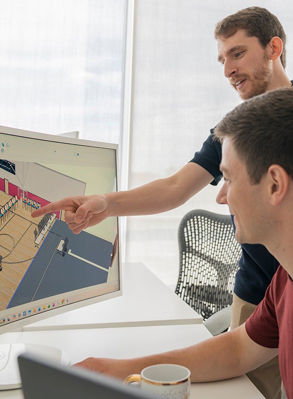 Student working at a computer with a floorplan on the computer screen and a teacher behind directing the student.