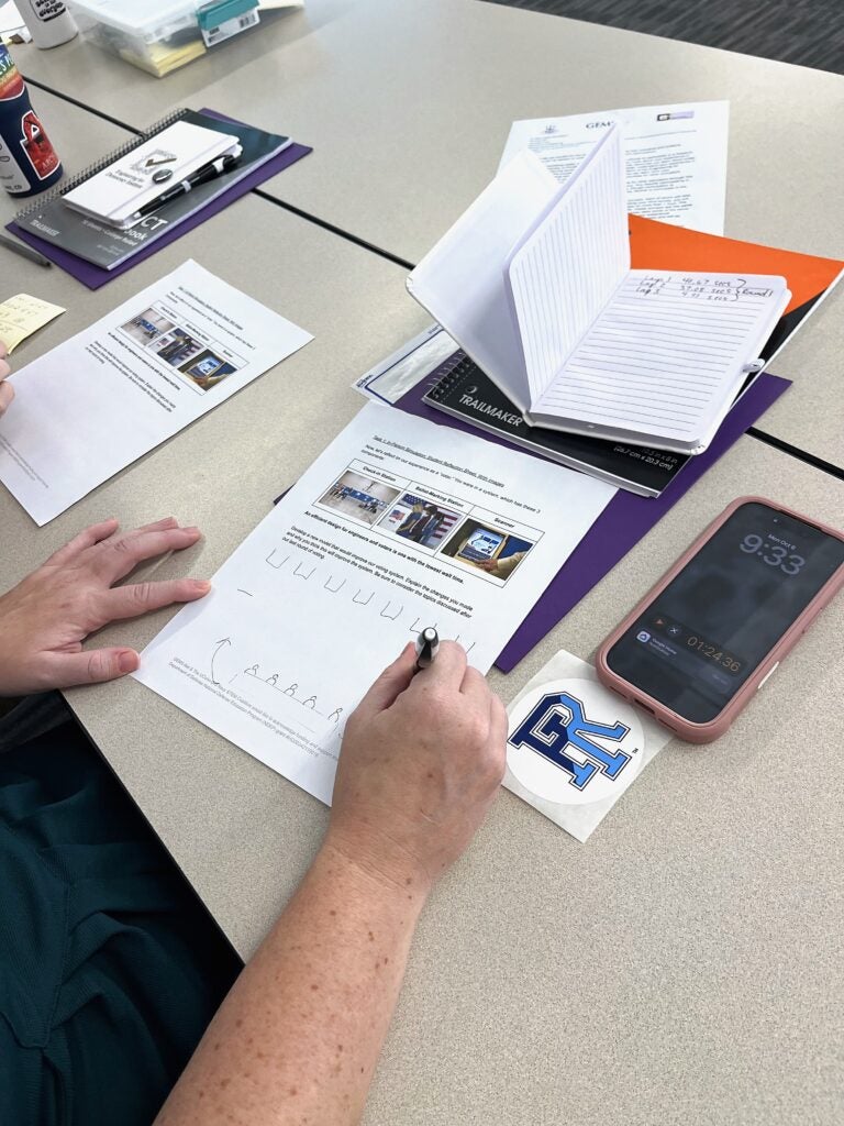 Close-up of hands sketching a polling-place redesign on a simulation reflection worksheet