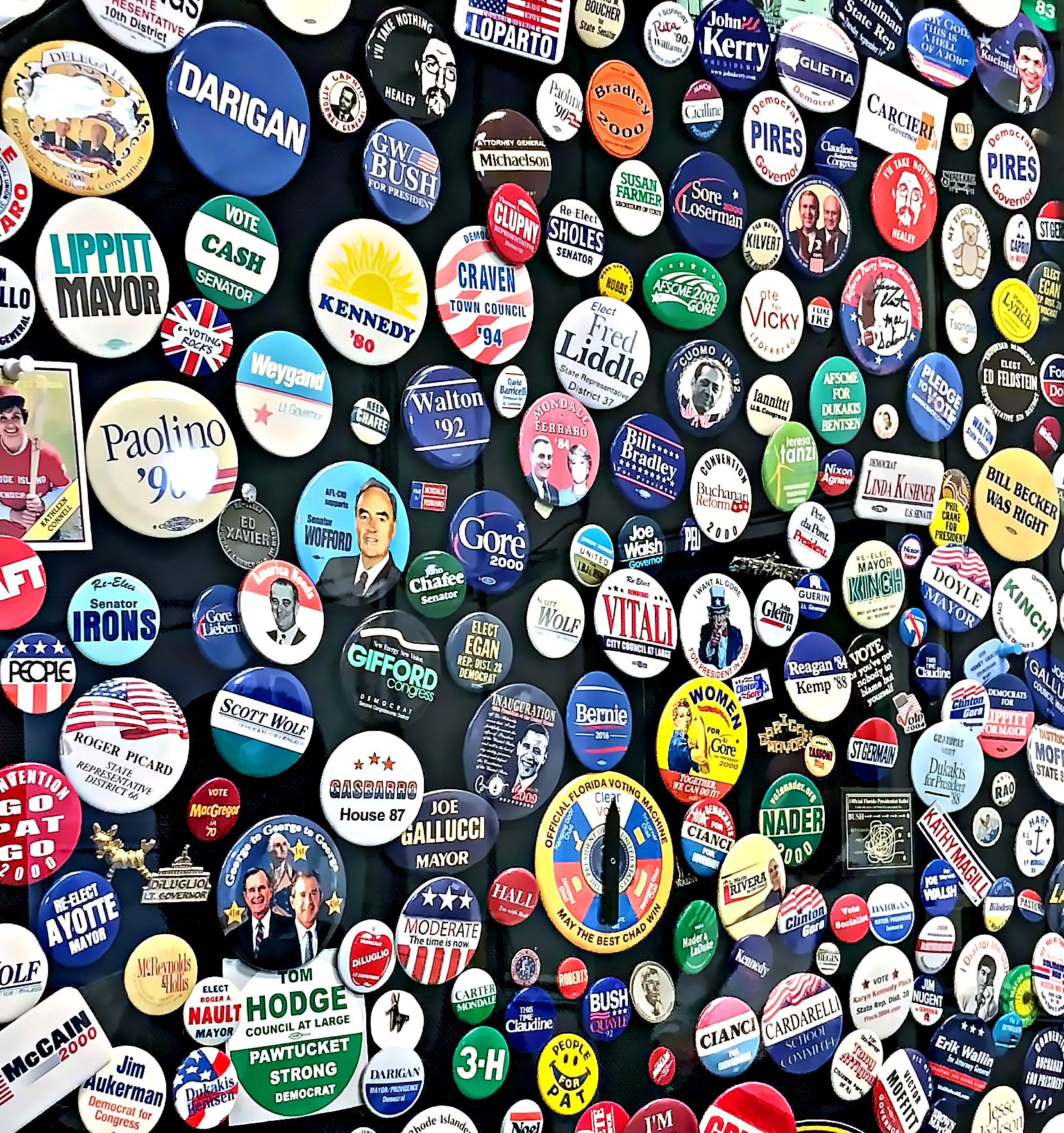 A tightly packed display of hundreds of political campaign buttons on a dark board, featuring candidates like Kennedy, Gore, and local Rhode Island races.